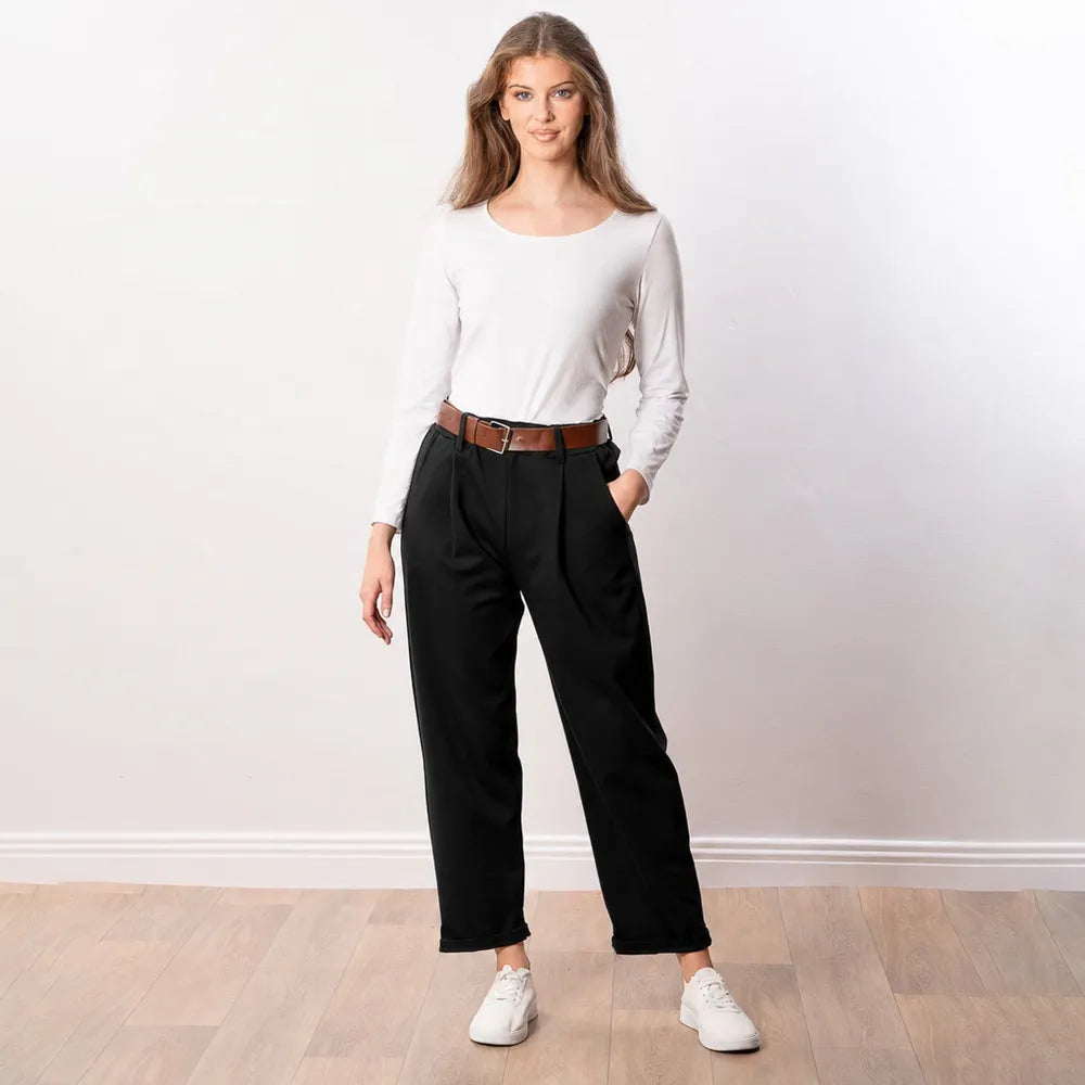 Black Arya tapered trousers styled with a white top and tan belt, relaxed front pose with one hand in pocket