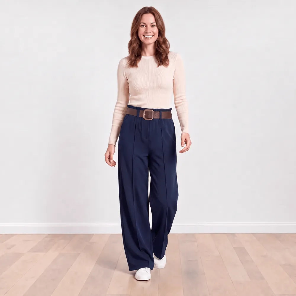 Smiling model stepping forward in navy Ellana wide-leg trousers with cream ribbed knit top, brown belt and white trainers