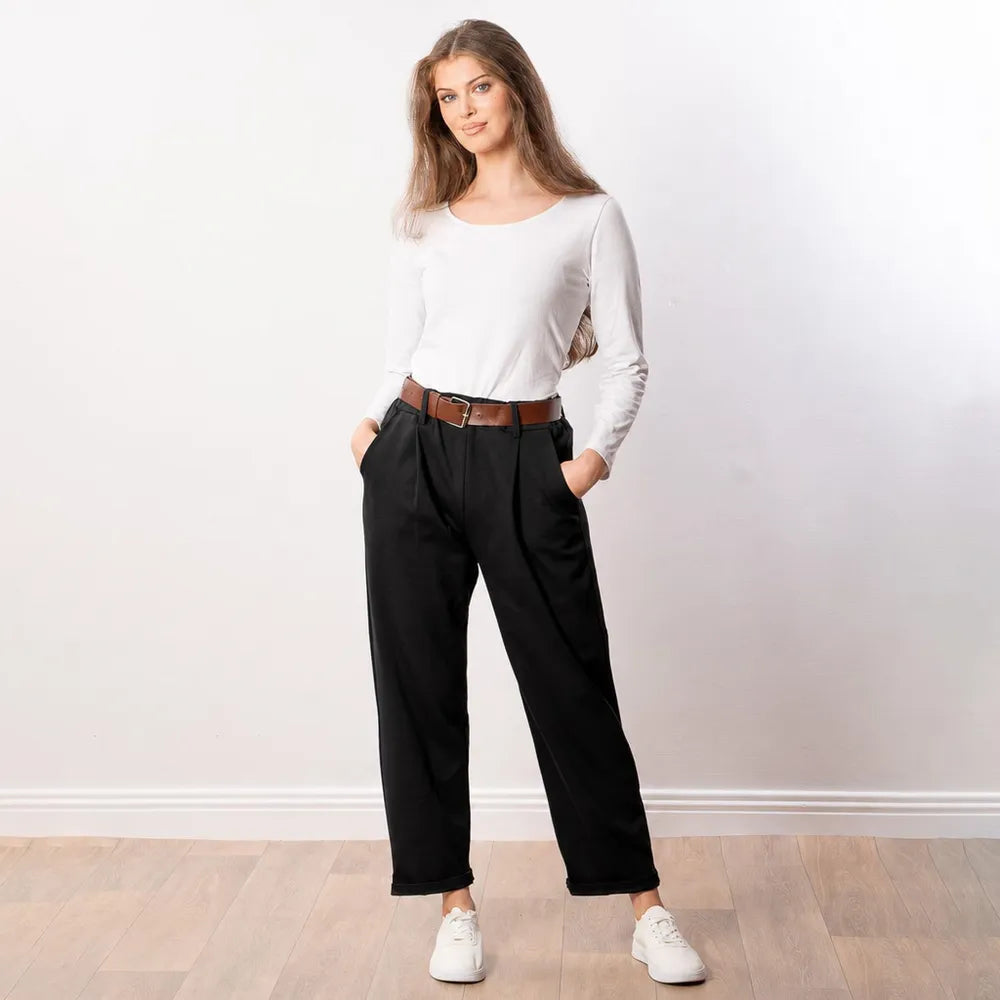 Black Arya tapered trousers front view showing side pockets, pleat detail and turned-up hem with white trainers