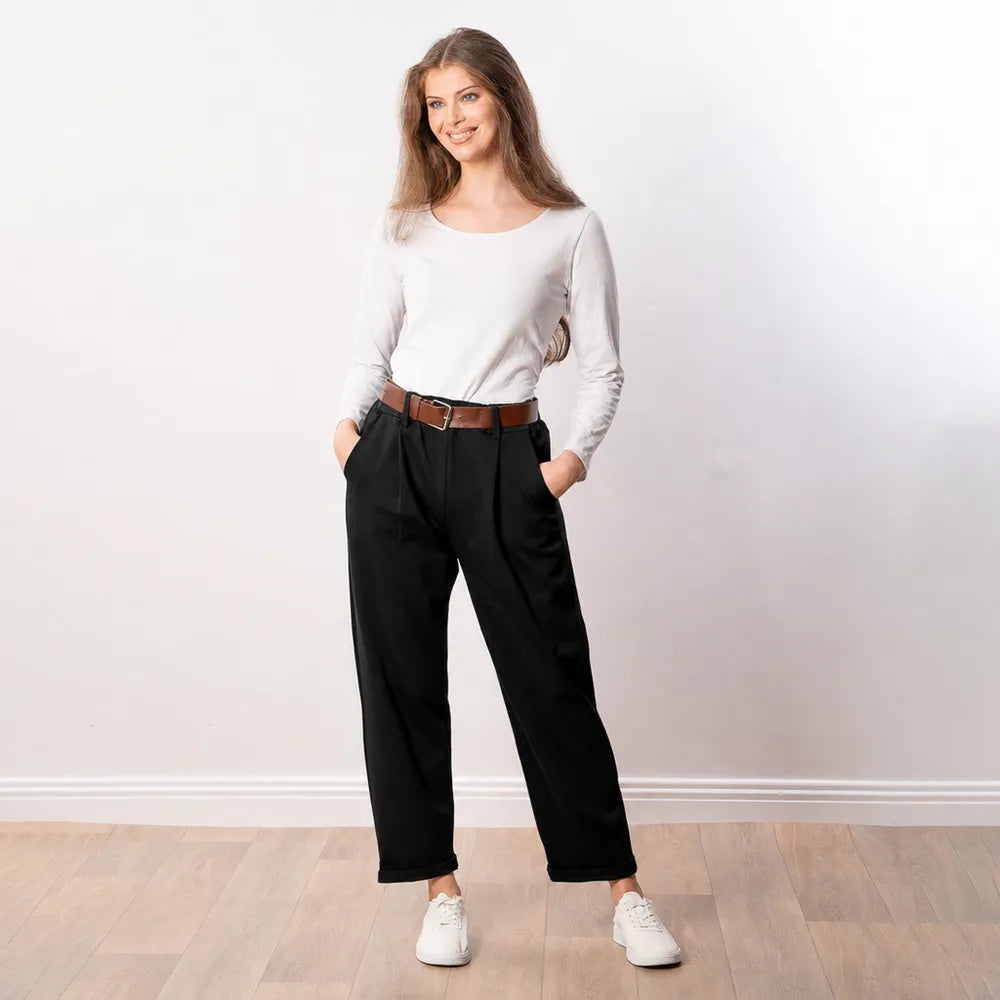 Cheerful woman wearing black Arya tapered trousers with a white long-sleeve top, tan belt and white trainers