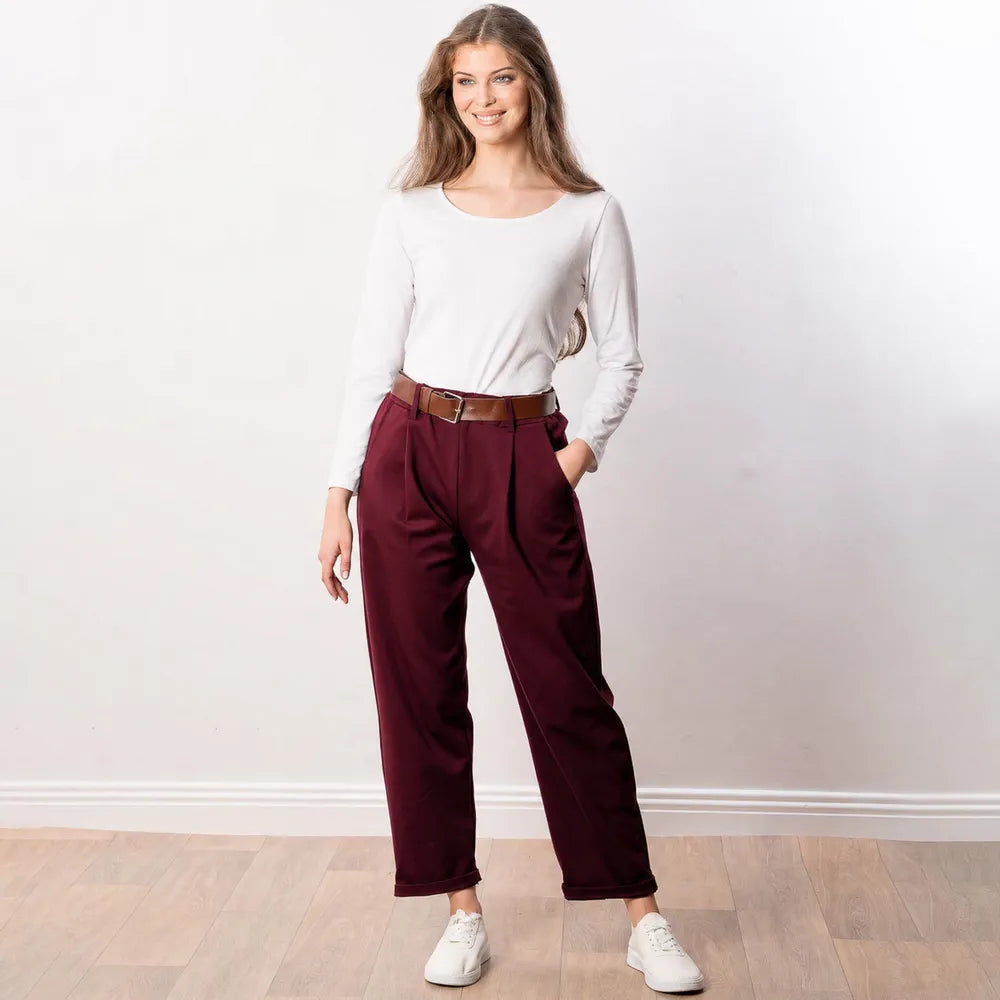 Arya Tapered Trousers in wine — smiling front view with hand in pocket, showing pleated waist and turned-up cuffed hem