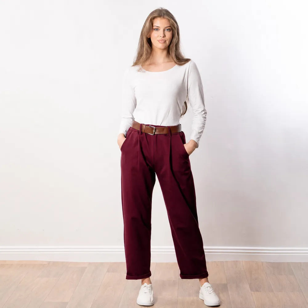 Arya Tapered Trousers in wine — front view with both hands in side pockets, brown belt at the elasticated waistband