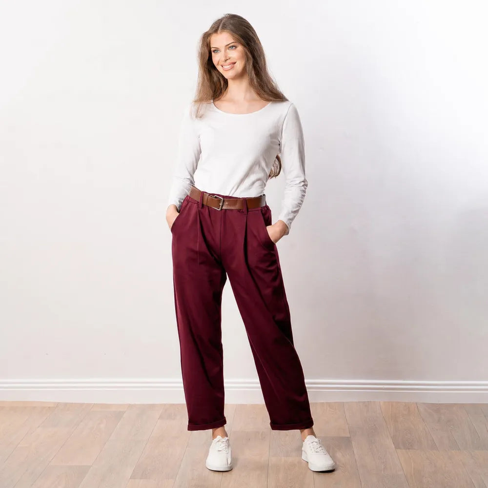 Arya Tapered Trousers in wine — cheerful front view with hands in pockets and white low-top trainers