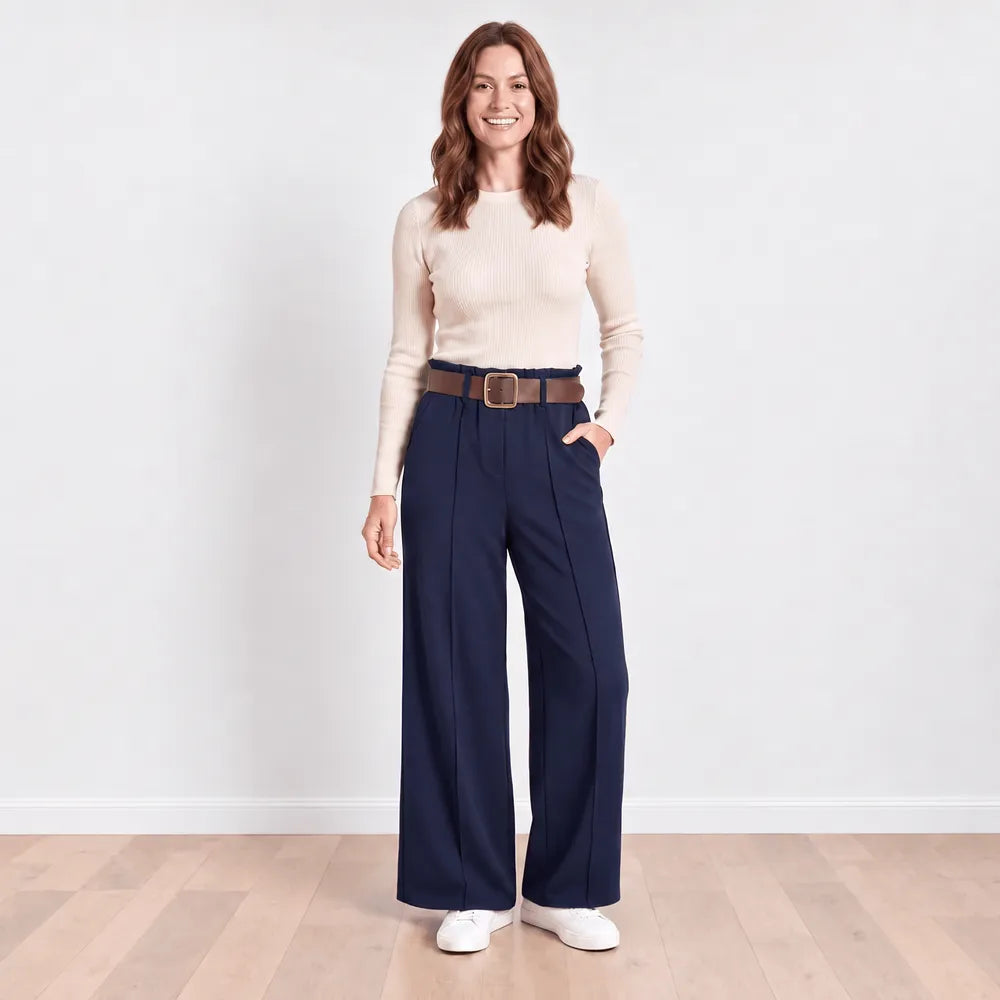 Navy Ellana wide-leg trousers front view with hand in the side pocket, worn with cream ribbed knit top and white trainers