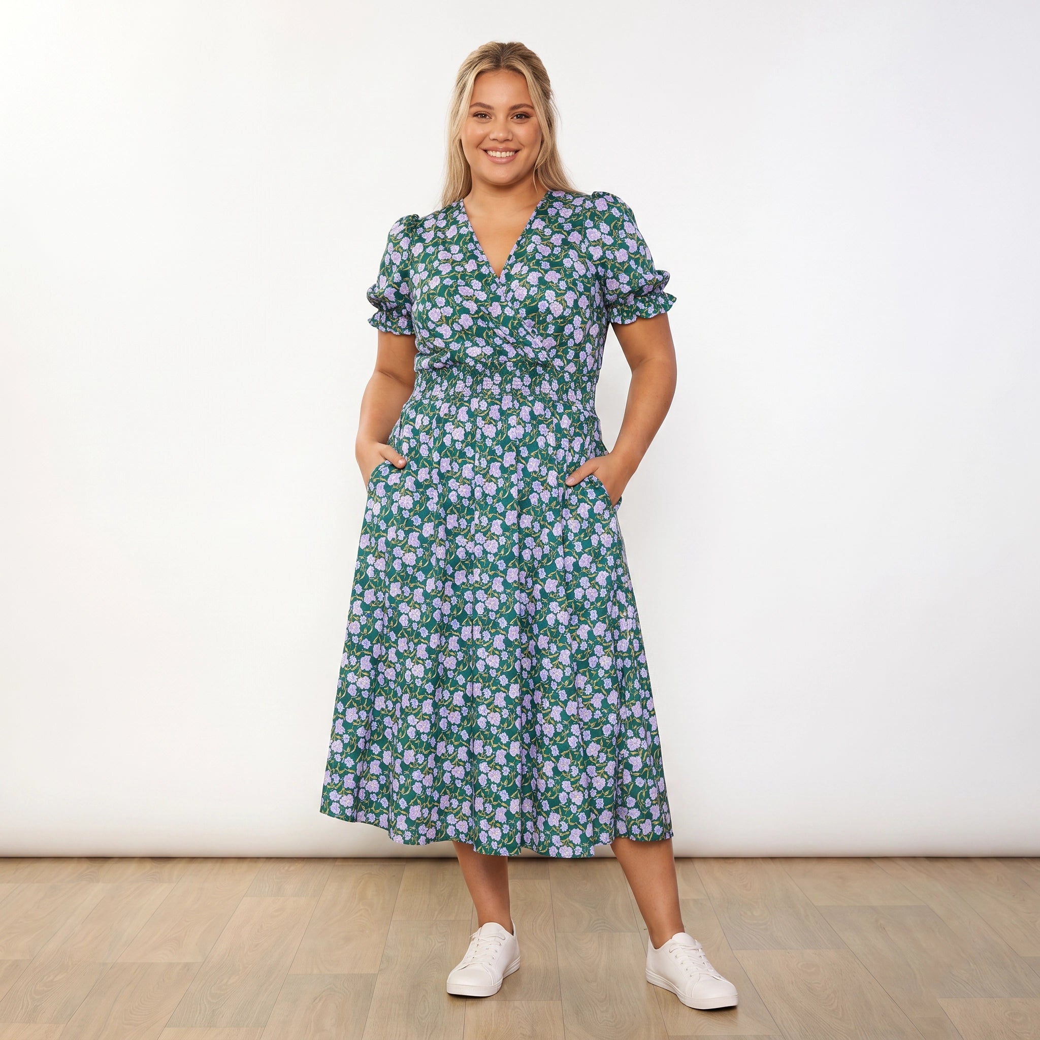 Belle Dress Green Lilac Wildflower - plus size model front, hands in pockets, warm smile
